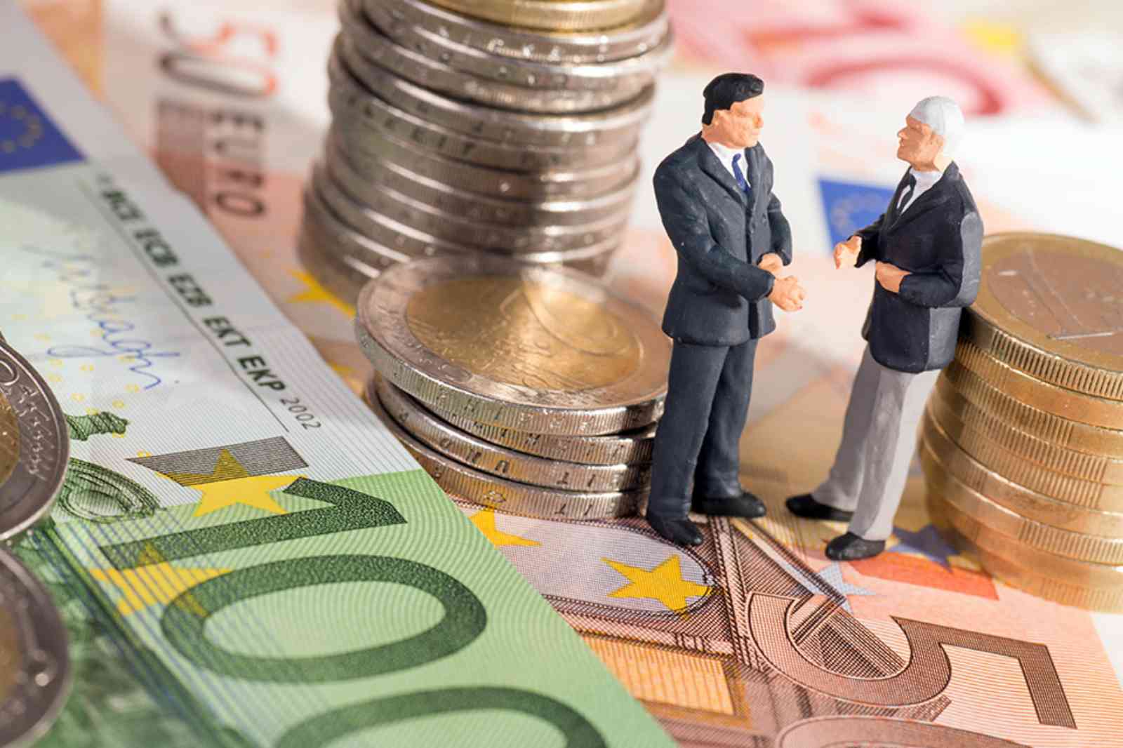 Zwei kleine Figuren stehend auf Geldscheine umringt von Münzen 